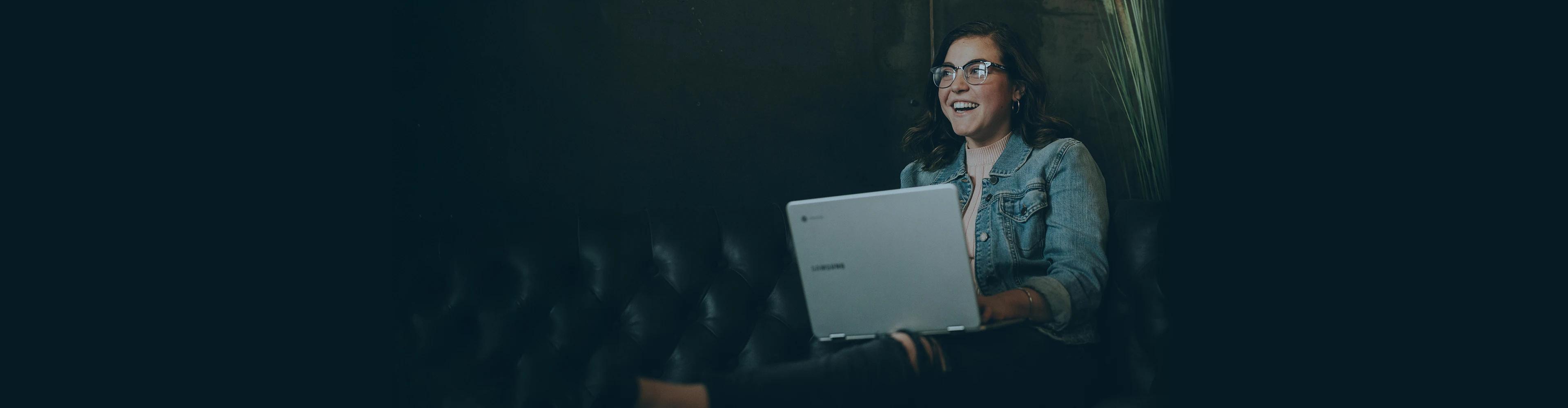 Professional with glasses smiling while using a laptop in a modern dark-themed environment